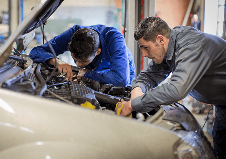 Deux apprentis mécanicien de l'École des Métiers examinent le moteur d'un véhicule. 